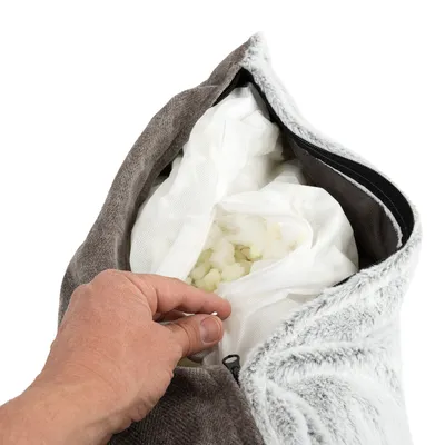 Hand öffnet Reissverschluss eines grauen Kissens mit herausnehmbarer Füllung aus weissem Schaumstoff in einem Netzbeutel.