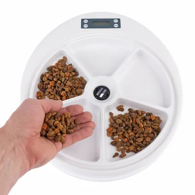 Voerdispenser met vier vakken, gevuld met droogvoer. Hand neemt voer uit een vak. Digitale display en bedieningsknoppen zichtbaar.