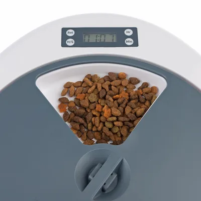 Automatische voerdispenser met digitale tijdsaanduiding en droogvoer in de container. Knoppen voor reset, uren en minuten zichtbaar.