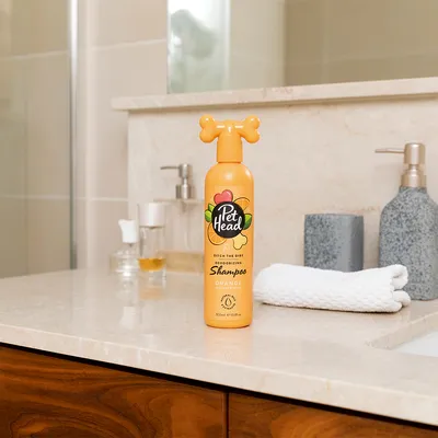 Flacone di shampoo Pet Head Ditch the Dirt Deodorizing, Orange con tappo a forma di osso, 300 ml, su piano bagno. Testo visibile: 'Shampoo Orange with Aloe'.