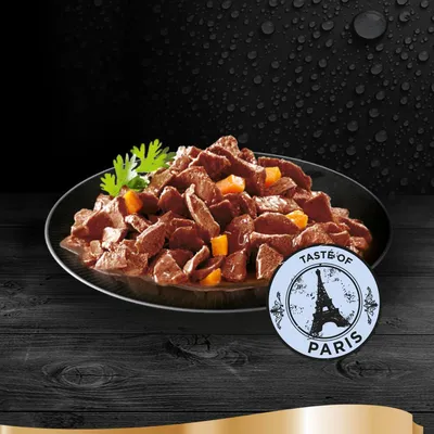 Tallerken med stykker af vådfoder og orange grøntsager, pyntet med persille. Rundt mærke med teksten 'Taste of Paris' og Eiffeltårn-motiv synligt foran tallerkenen.