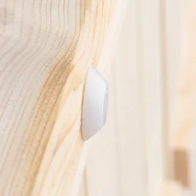 Détail d’un élément en bois clair avec un patin ou embout en plastique blanc fixé sur la surface.