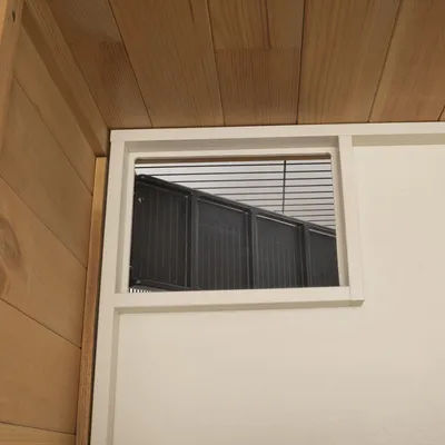 Vista interna di una struttura in legno con apertura finestra e elementi a griglia neri.