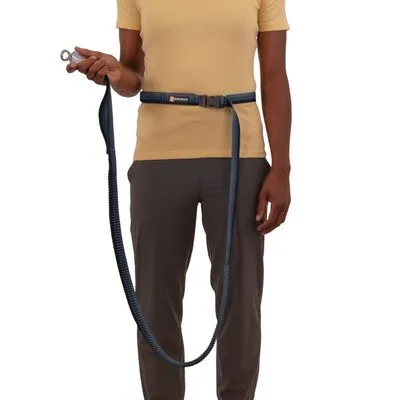 Persoon draagt een Ruffwear heupgordel met bevestigde hondenriem van donker textiel, metalen haak zichtbaar in hand.