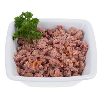 Miska z rozdrobnioną mokrą karmą, widoczne kawałki mięsa i marchewki, udekorowana świeżą pietruszką.