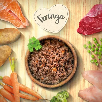 Feringa mokra karma w drewnianej misce, otoczona składnikami: łosoś, wołowina, kurczak, ziemniaki, marchew, brokuły i groszek. Widoczne serduszkowe logo Feringa.