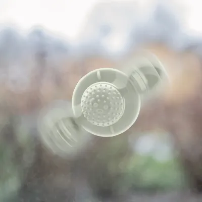 Jouet pour animaux en plastique blanc avec ventouse, fixé sur une vitre. Partie centrale texturée à picots visibles.