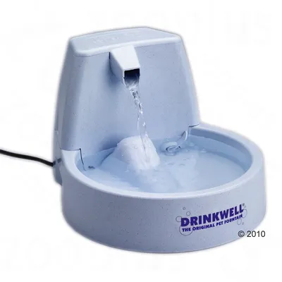 Fontaine à eau pour animaux en plastique, marque Drinkwell, avec jet d’eau central et branchement électrique visible. Texte sur le produit : DRINKWELL THE ORIGINAL PET FOUNTAIN.