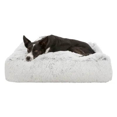 Cama rectangular para perro de tela gris claro, con un perro tumbado encima. La superficie parece mullida y suave.