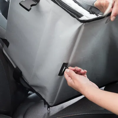 Hand fastening seat belt to grey transport box in car. Close-up of fastening loop.