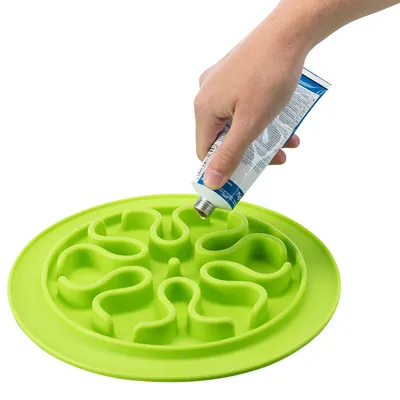 Hand applying paste to a green lick mat with wavy pattern.