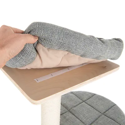 Hand zeigt abnehmbares, gepolstertes Kissen mit Klettverschluss auf einer Holzplattform eines Kratzbaums.