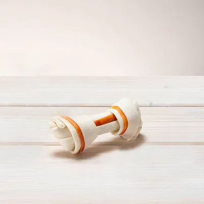 Žvečilna kost iz belega materiala z oranžnimi poudarki, primerna kot žvečilni izdelek za pse.