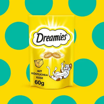 Dreamies, mit köstlichem Käse, 60g. Envase amarillo con ilustración de queso y un gato jugando. Texto en alemán visible en el paquete.