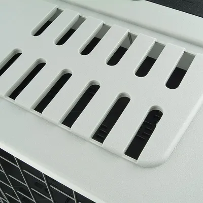 Dettaglio delle fessure di ventilazione sulla parte superiore di un trasportino per animali in plastica, con griglia visibile sul lato.