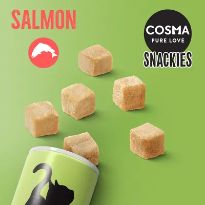 COSMA PURE LOVE SNACKIES, SALMON. Flera kubformade bitar samt en grön förpackning med kattmotiv syns. Texten 'SALMON' och fiskikon är tydligt synliga.