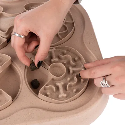 Hand places food piece into interactive toy with maze design for slow feeding.