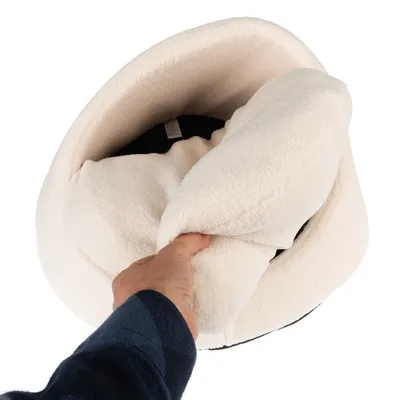 Hand zeigt die weiche, cremefarbene Innenseite eines Haustierbetts mit schwarzem Boden.