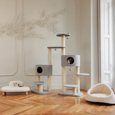 Cat tree with multiple levels, sisal posts and grey resting surfaces. Two caves with round entrances and hanging play balls. Cat bed on the left, cosy cave on the right.