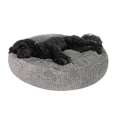 Zwarte hond ligt uitgestrekt op een rond, grijs knuffelbed met een zachte structuur.
