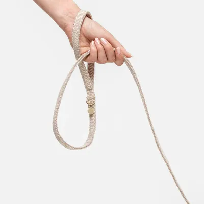 Beige fabric dog lead with herringbone pattern, held by a hand. Metal ring and tag visible.