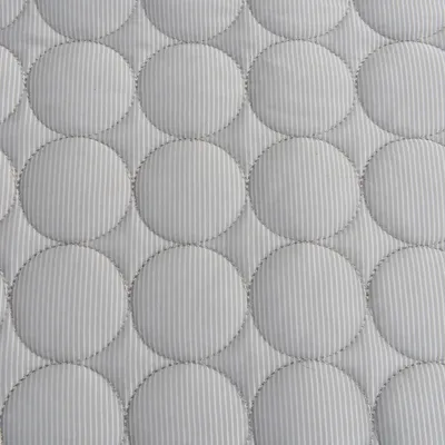 Zbliżenie na pikowany wzór tkaniny z okrągłymi przeszyciami w kolorze białym i szarym.