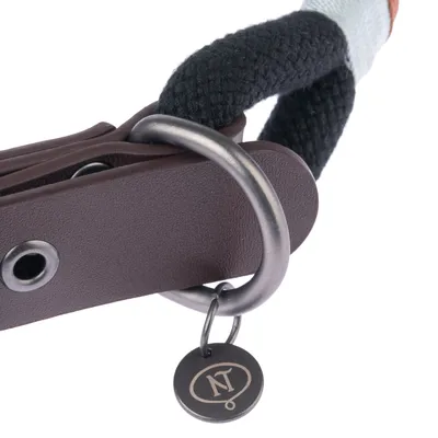 Close-up of a brown leather collar with metal ring and pendant featuring NT logo. Black rope visible as part of the design.