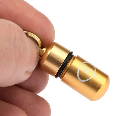 Goldfarbener Metall-Anhänger mit Schraubverschluss und eingraviertem Symbol, gehalten zwischen Daumen und Finger.
