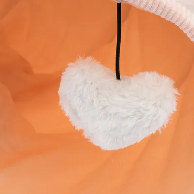 Bílé plyšové hračky ve tvaru srdce na černé šňůrce před oranžovým pozadím.