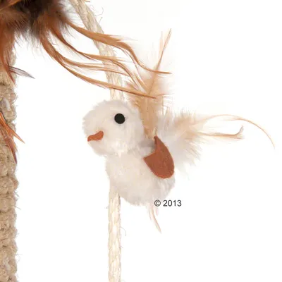 Kattelegetøj formet som en lille fugl med hvid plys, brune filtpletter og fjer, hængende i en snor på et kradsetræ. Materialer: plys, filt, fjer, reb.