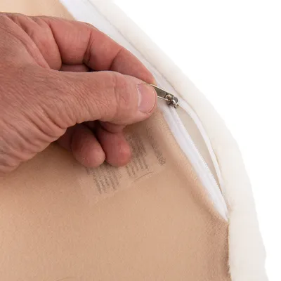 Nahaufnahme einer Hand, die einen Reissverschluss an einem beige-weissen Stoff öffnet. Detail zeigt die Funktion des abnehmbaren Bezugs.