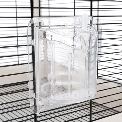 Bac transparent en plastique fixé sur les barreaux d'une cage, compartimenté à l'intérieur, sans marque visible ni texte.