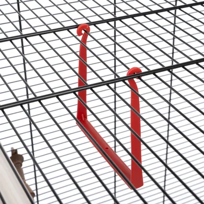 Support rouge en plastique fixé sur les barreaux d'une cage métallique, vu de dessus. Aucun autre accessoire ou animal visible.