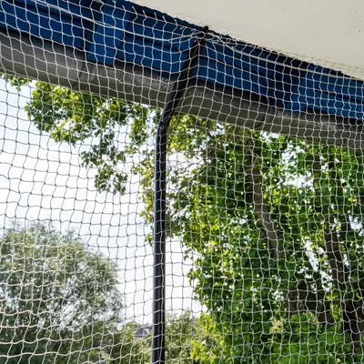 Bezpečnostná sieť na balkón, pripevnená na modrej kovovej tyči. V pozadí zelené stromy a obloha.