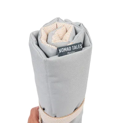 Zusammengerollte graue Decke mit beige-weissem Muster, Label 'Nomad Tales München' sichtbar.