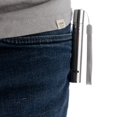 Silver-coloured laser pointer with wrist strap, attached to a trouser pocket.