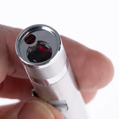 Close-up of a silver laser pointer with red light, held between two fingers.