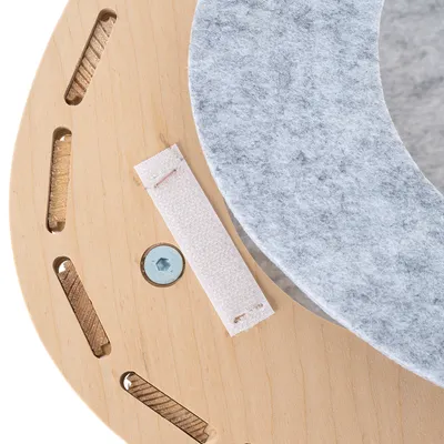 Détail d’un support en bois clair avec vis, bande auto-agrippante blanche et coussin rond en feutre gris. Matériaux visibles : bois, métal, feutre, tissu.