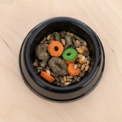 Sort skål med en blanding af korn, piller og farverige godbidder i grøn og orange.