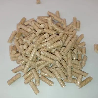 Hoop beige cilindervormige pellets op een witte ondergrond, losse korrels zichtbaar. Materiaal lijkt geperst hout of plantaardig vezel. Geen merknaam of tekst aanwezig.