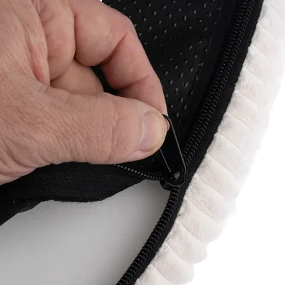 Gros plan sur une main ouvrant une fermeture éclair noire sur un tissu noir à pois et bordure beige, montrant la finition du produit textile.
