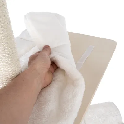 Hand showing removable white plush cushion with Velcro fastener on a wooden platform next to a sisal scratching post.