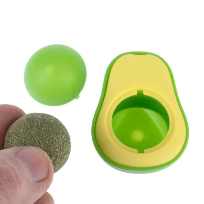 Jouet vert et jaune en forme d’avocat avec inscription « TOYS avocado », deux boules incluses, une verte et une marron tenue par une main, matériaux plastique et matière végétale visibles.