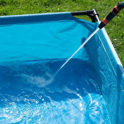 Piscina retangular azul para animais de estimação a ser enchida com água através de uma mangueira, estrutura visível em tubos pretos.