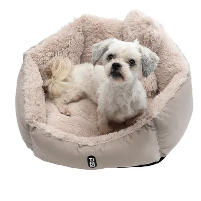 Dog sitting in a beige, fluffy dog bed with Tiaki logo on the front.