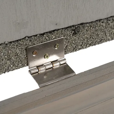 Närbild av ett metallgångjärn som förbinder två träplattor. Ovansida med synlig grusbeläggning.