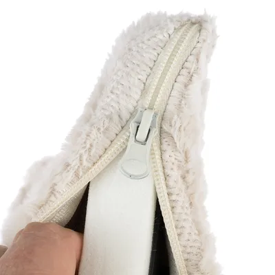 Gros plan sur une housse en tissu peluche beige avec fermeture éclair ouverte, montrant la mousse intérieure et une main tenant le bord.