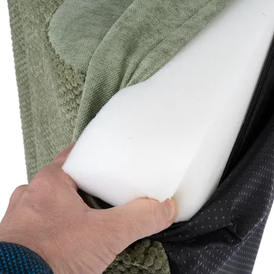 Närbild av en hand som visar kuddkärnan av skumgummi, omgiven av grön tygklädsel och svart dragkedja.