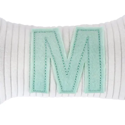 Bijeli jastuk sa zelenim filcanim slovom 'M' na prugastoj površini.