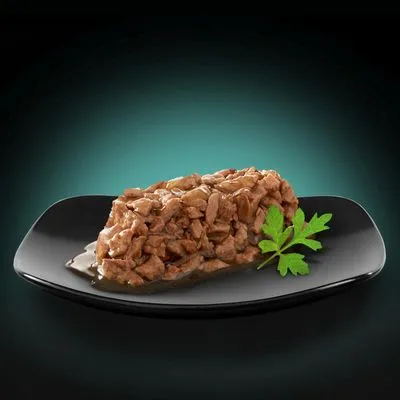 Portie natvoer met stukjes vlees in saus, geserveerd op een zwart bord met peterselie als garnering. Merk- of productnaam niet zichtbaar.